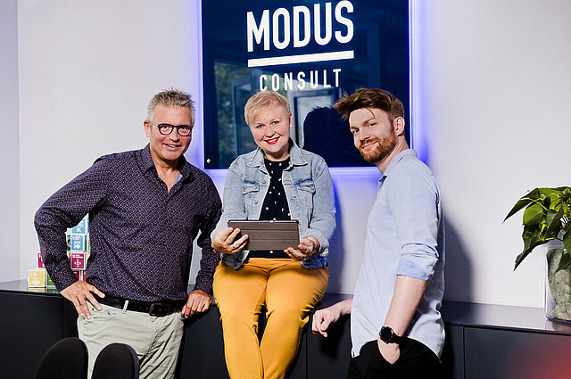 Jobs bei MODUS Consult. Zwei Kollegen und eine Kollegin lächeln freundlich in die Kamera.