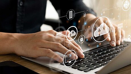 Erfolgsfaktor Cloud. Microsoft Dynamics 365 cloudbasiert. Bild mit Mensch, der vor einem Laptop sitzt. Grafisch dargestellt Cloud-Wolken schweben über dem Laptop.