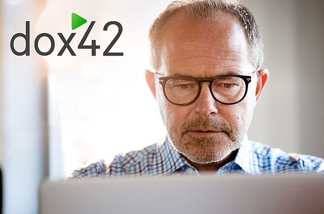 Kollege, der freundlich auf seinen Laptop schaut. In der linken Ecke des Bildes ist das Logo von dox42 zu lesen.