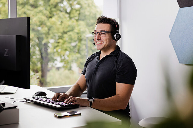 Freundlicher Mitarbeiter von MODUS Consult steht an seinem Arbeitsplatz und schaut auf einen Monitor.
