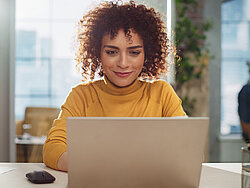 Sympathische Frau, die lächelnd auf ihren Laptop schaut.
